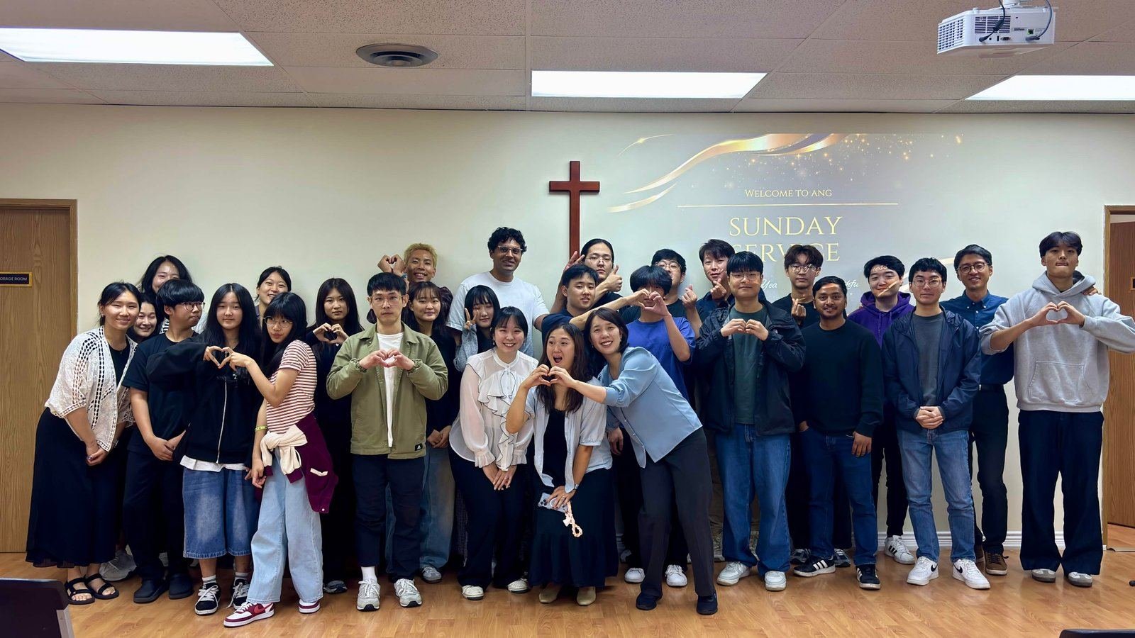 The Vancouver congregation, about forty young adults, standing in rows in a chapel under a wooden cross, many making heart signs with their hands